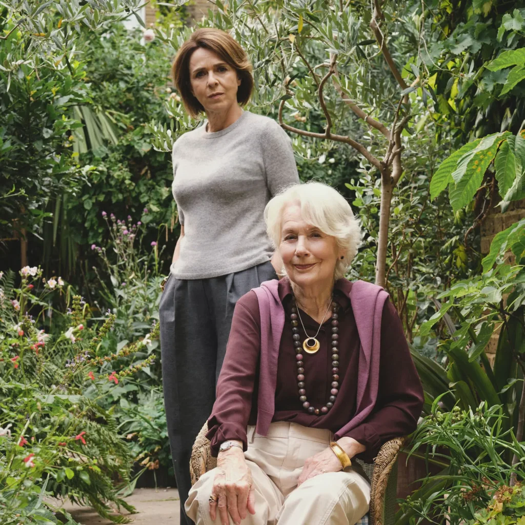 Meredith: two women in a leafy garden, one standing, one seated in a wicker chair